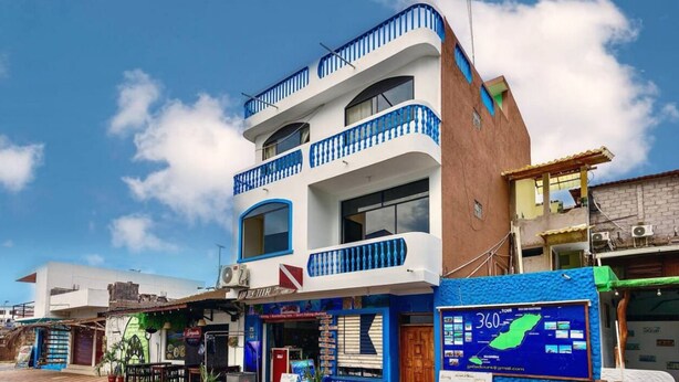 A multi-story building with balconies, a storefront with a sign, and a blue awning. - Blue Horizon, Galápagos (San Cristóbal)