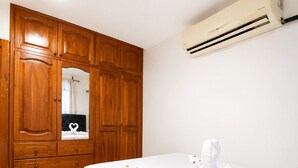 A bedroom with a bed, a wooden wardrobe, a mirror, and an air conditioning unit. - Blue Horizon, Galápagos (San Cristóbal)