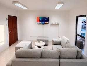 A modern living room with a grey sofa, a round coffee table, and a flat-screen TV mounted on the wall.