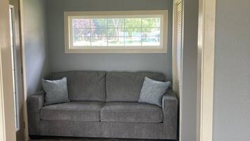 Una habitación con un sofá gris, una ventana con persianas y un ventilador de techo.