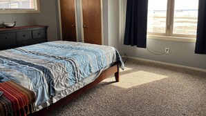 Un dormitorio con cama, cómoda, dos puertas, ventana con cortinas y vista a la playa.