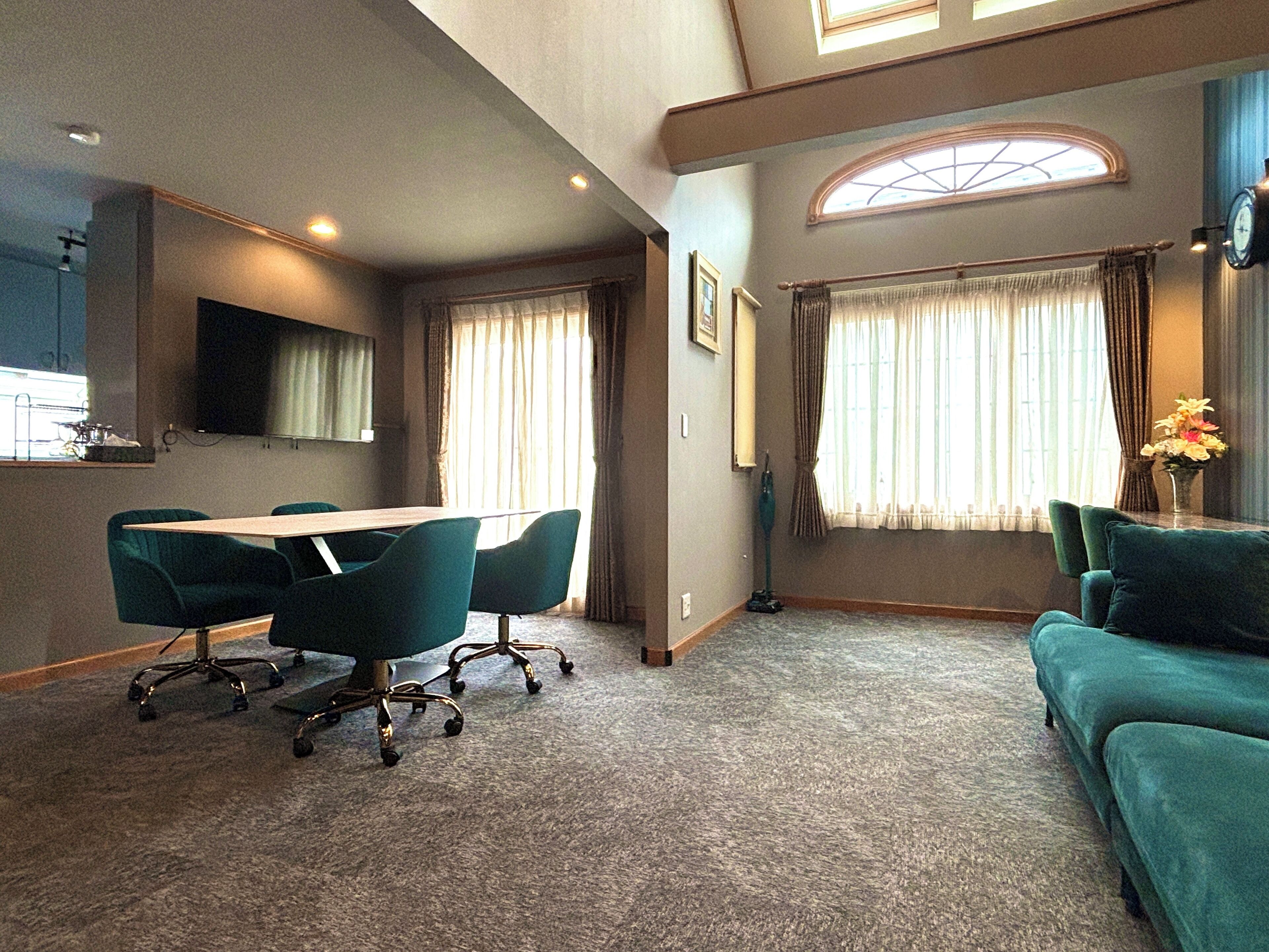 A room with a dining table, chairs, a sofa, and a large window with curtains.