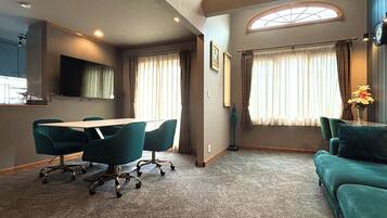 A room with a dining table, chairs, a sofa, and a large window with curtains.