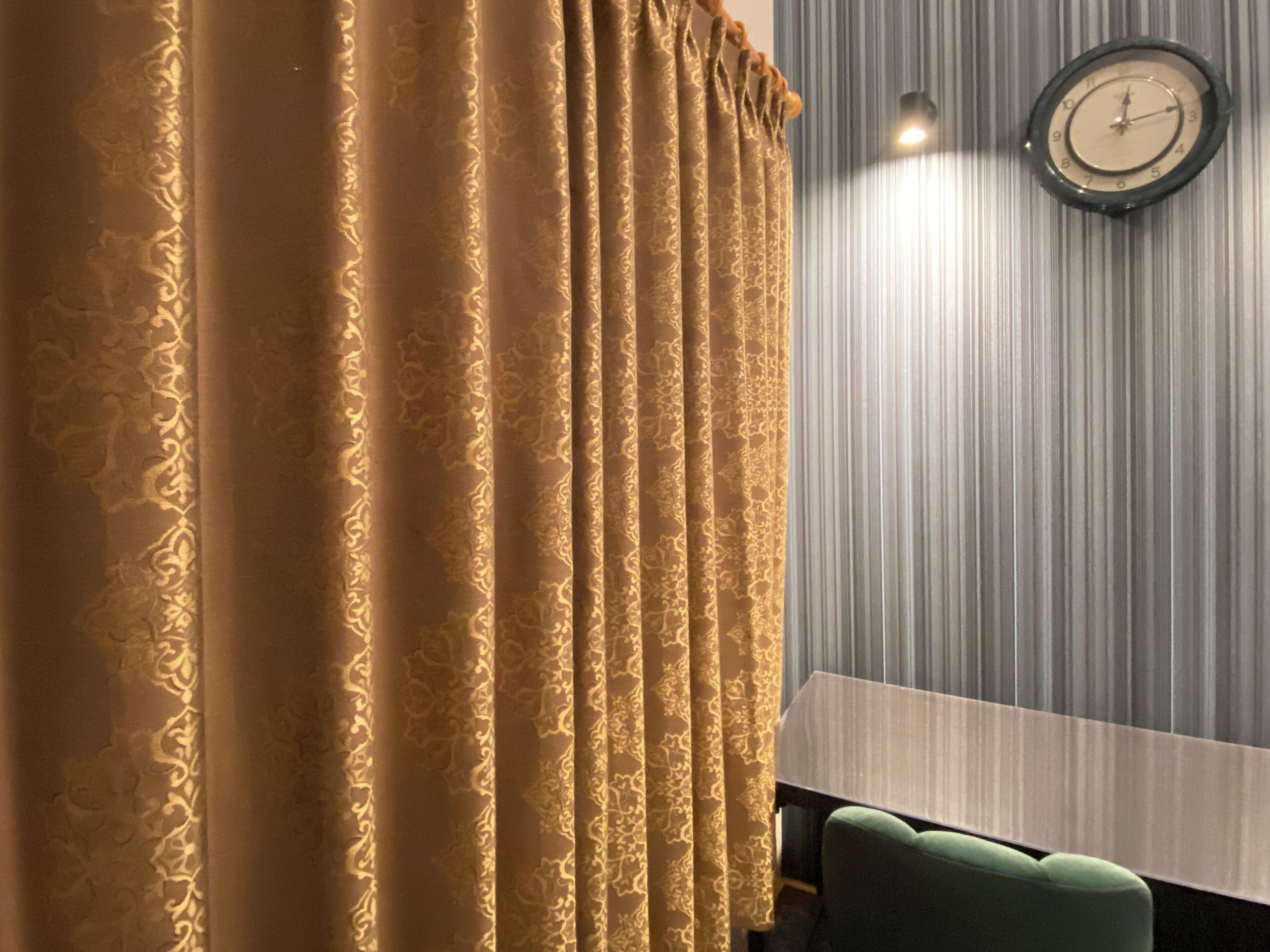 A room with a patterned curtain, a clock on the wall, and a green chair.