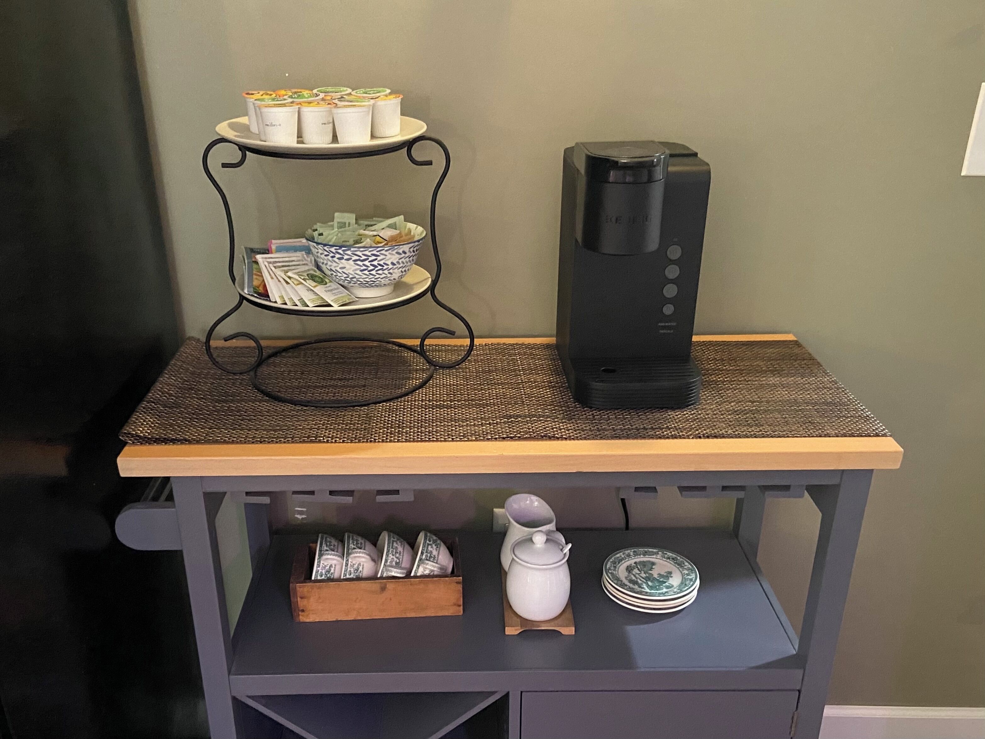 A kitchen counter with a coffee maker, a tray of food containers, a bowl, and a stack of plates.