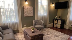 A living room with a sofa, a chair, a small table with a plant, a decorative wall piece, a television, and a cabinet.