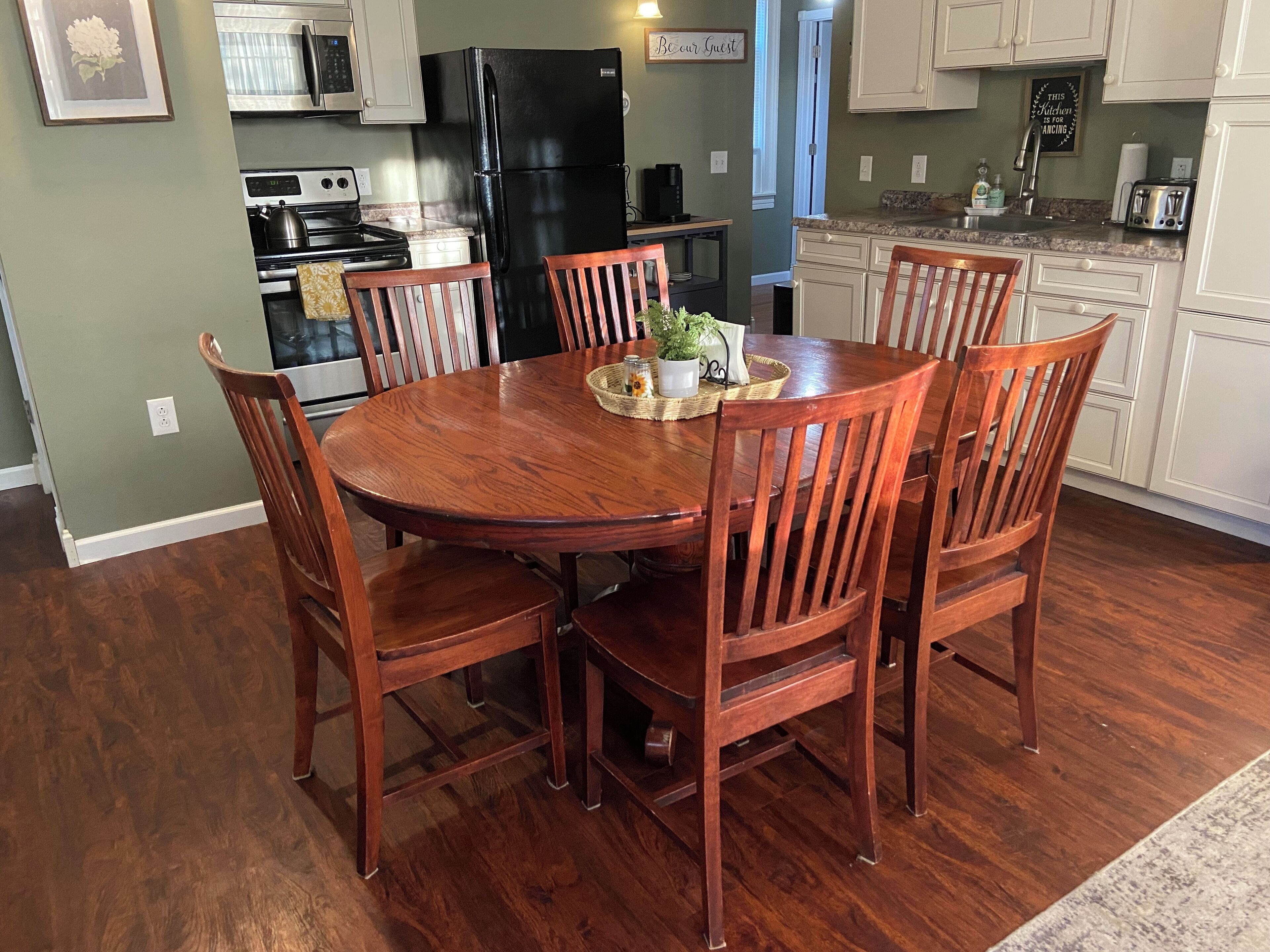 A dining area with a wooden table and chairs, a black refrigerator, a microwave, and a stove in the background.