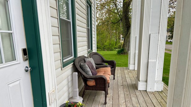 A porch with a wicker chair, a potted plant, and a door.