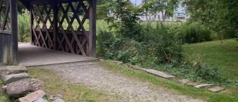 A wooden pavilion with a lattice roof, surrounded by grass and a stone pathway.