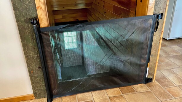 A room with a wooden floor, a door with a black mesh screen, and a tiled wall.