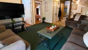A living room with a large flat-screen TV, two sofas, a coffee table, and a wooden ceiling.