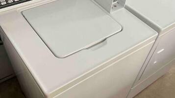 Eine weiße Waschmaschine, vorne gesehen, mit Bedienfeld und einer Klappe zum Beladen von oben.