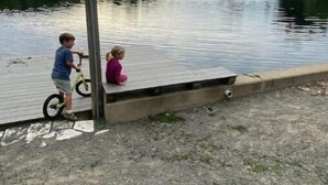 A dock with a sign reading "N's Dock" by a calm lake with a fountain in the background.