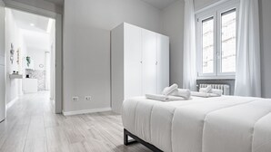 Une chambre à coucher avec un lit, une armoire blanche et une vue sur la ville par la fenêtre.