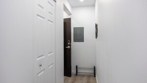 Un couloir étroit aux murs blancs, avec un plancher en bois, une porte blanche et un petit radiateur.