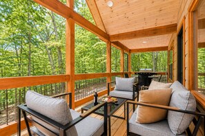 A covered outdoor seating area with wooden beams, a grill, and a view of a forest. - Your Fall Getaway is here - Modern Luxury Cabin -  Kings Beds - Hot tub (Cherry Log)