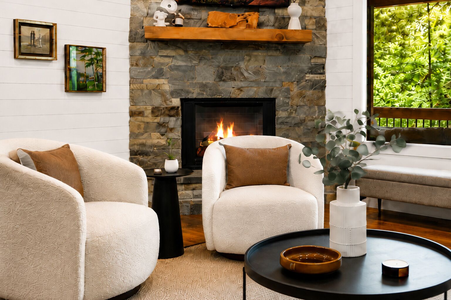 A living room with a stone fireplace, two armchairs, a side table, and a view of greenery through a window.