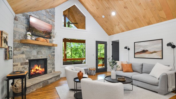 A spacious living room with a stone fireplace, wooden ceiling, and large windows offering a view of the outdoors. - Your Fall Getaway is here - Modern Luxury Cabin -  Kings Beds - Hot tub (Cherry Log)