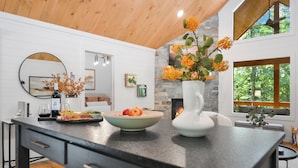 A modern kitchen with a large island, a stone accent wall, and a view of the outdoors. - Your Fall Getaway is here - Modern Luxury Cabin -  Kings Beds - Hot tub (Cherry Log)