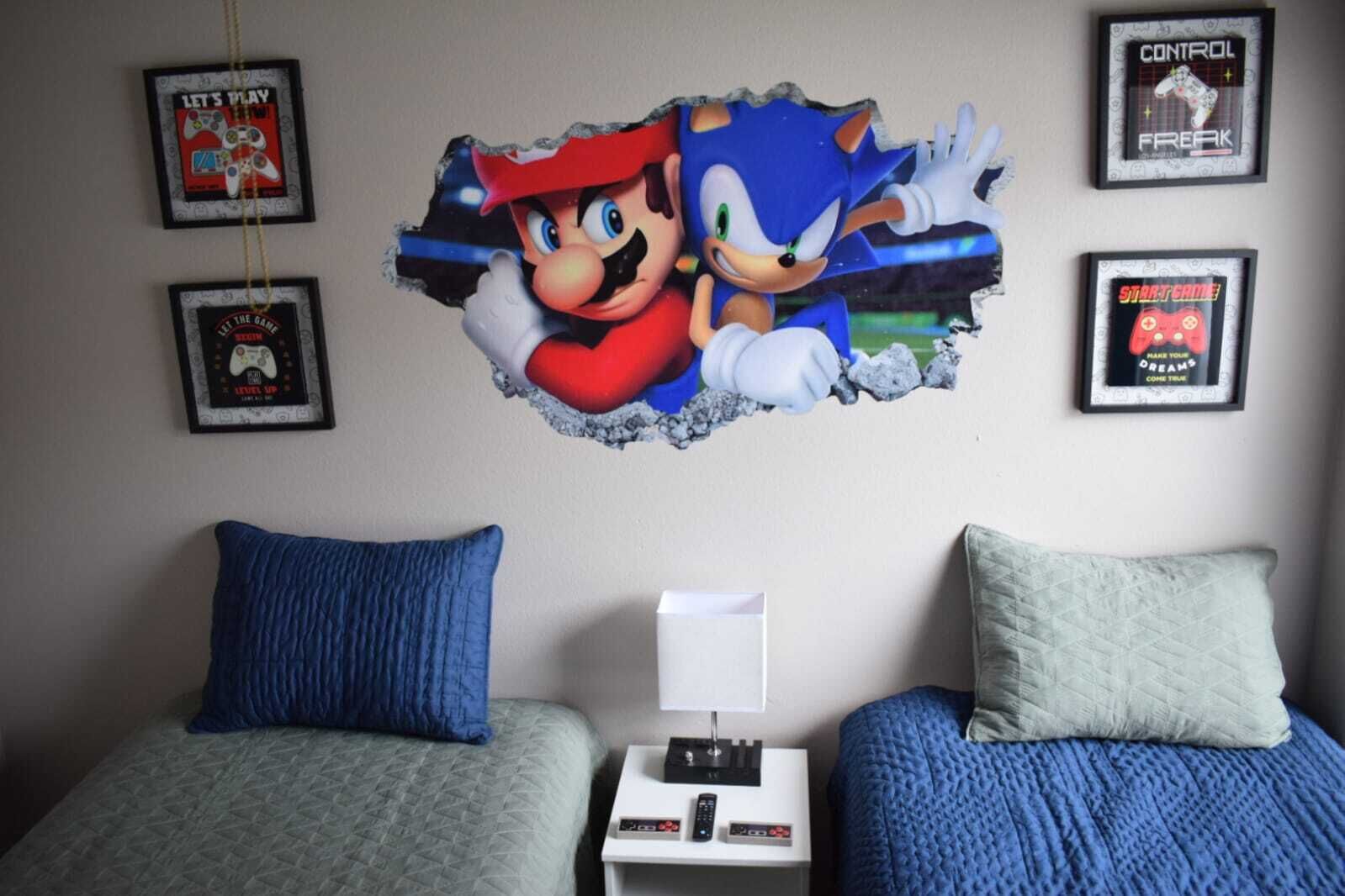 A bedroom with two beds, a nightstand, and framed posters on the wall.