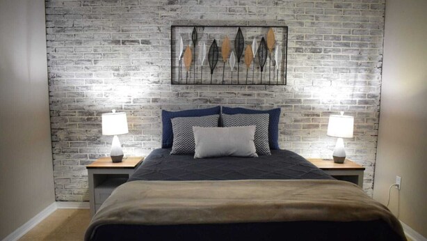 A bedroom with a brick wall, a bed with a dark headboard, two bedside tables with lamps, and a framed artwork above the bed. - Zojo_ Lovely House Close TO Disney (Clermont)