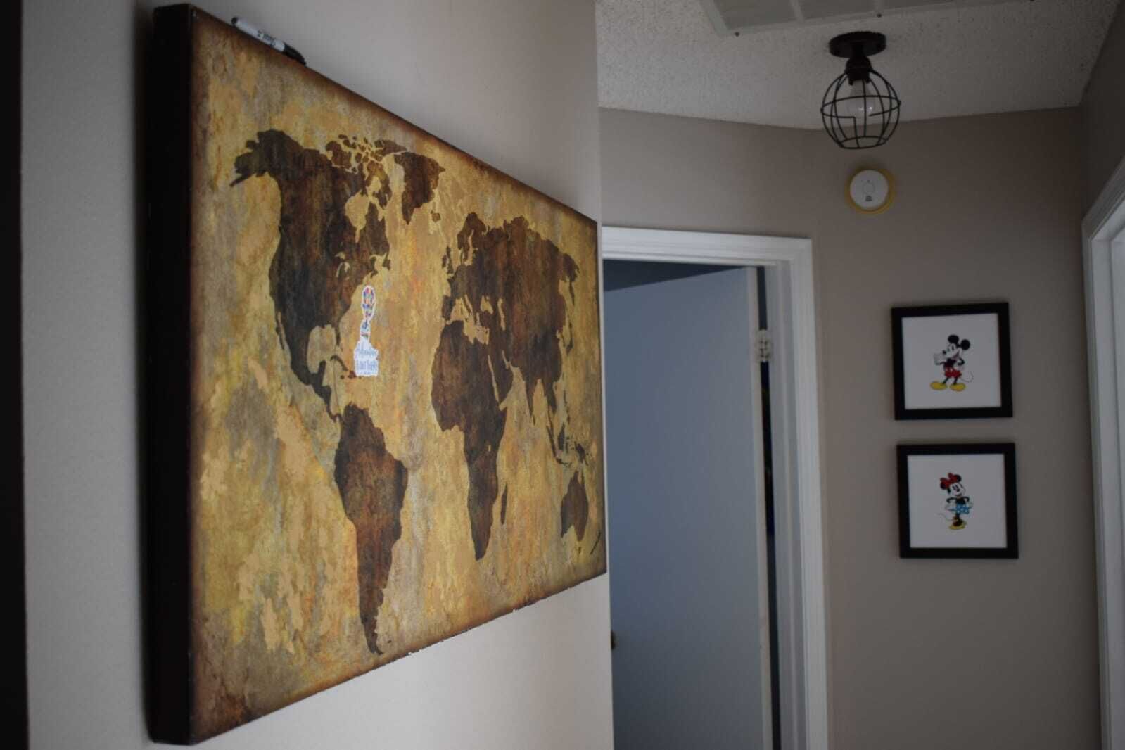 A room with a large world map artwork on the wall, a door, and two framed pictures of Mickey Mouse.