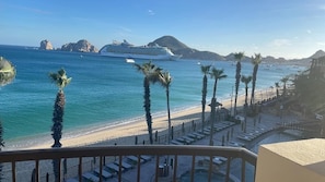 Enjoy breathtaking views of the ocean from your balcony, overlooking a serene beach lined with palm trees and a picturesque town in the distance.