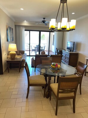 Relax in this open-plan living space with a dining area, featuring a glass-top table and comfortable seating.