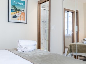Et hotelværelse med en seng, et badeværelse med brusekabine i glas og et plakatbillede af Cannes på væggen.