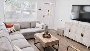 Ein modernes Wohnzimmer mit einem Ecksofa, einem Couchtisch, einem Fernseher und einer weißen Kommode.