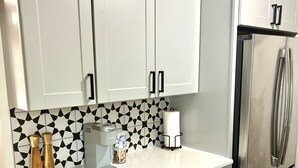 Eine Küche mit weißen Schränken, einem Edelstahl-Kühlschrank, einer Kaffeemaschine und einer geometrischen Fliesenrückwand.