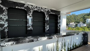 A modern outdoor kitchen with a black and white marble backsplash, a wooden deck, and a view of a residential area. - SOHO PV PUERTO VALLARTA  (Puerto Vallarta)