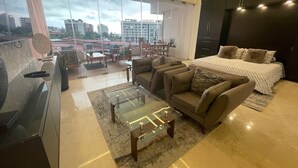 A modern living room with a sofa, a glass coffee table, and a bed with patterned bedding. - SOHO PV PUERTO VALLARTA  (Puerto Vallarta)