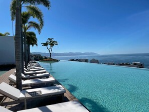 A infinity pool with lounge chairs and palm trees, overlooking a clear blue sea and distant mountains. - SOHO PV PUERTO VALLARTA  (Puerto Vallarta)