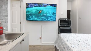A modern hotel room with a large flat-screen TV mounted on the wall, a bed with a patterned bedspread, a small kitchenette with a microwave, and a bathroom with a shower curtain. - #202_Downtown's Exquisite Luxury Studio (Montreal)