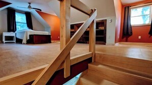 Una habitación con una escalera de madera, una cama y un ventanal con cortinas.