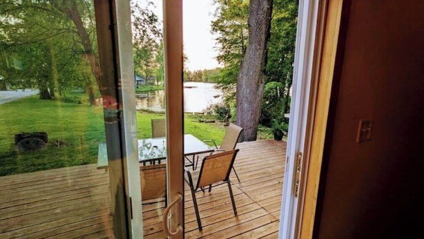 Terraza de madera con puerta de vidrio que da a una vista de un lago y follaje.