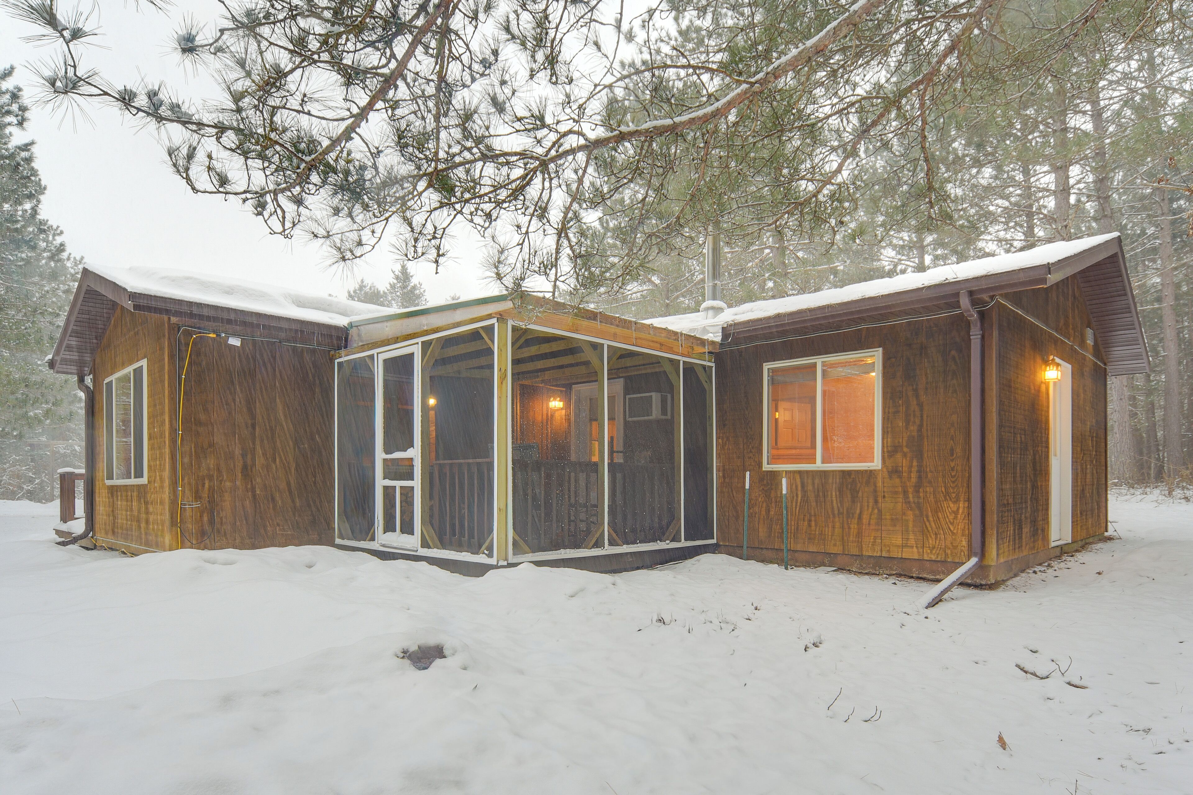 Une cabane en bois dotée d’une véranda grillagée, de grandes fenêtres et surplombant un paysage enneigé.
