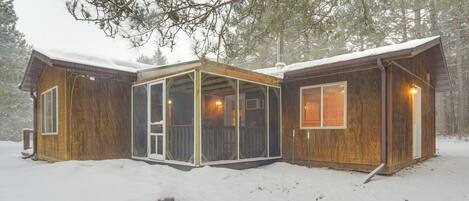 Une cabane en bois dotée d’une véranda grillagée, de grandes fenêtres et surplombant un paysage enneigé.