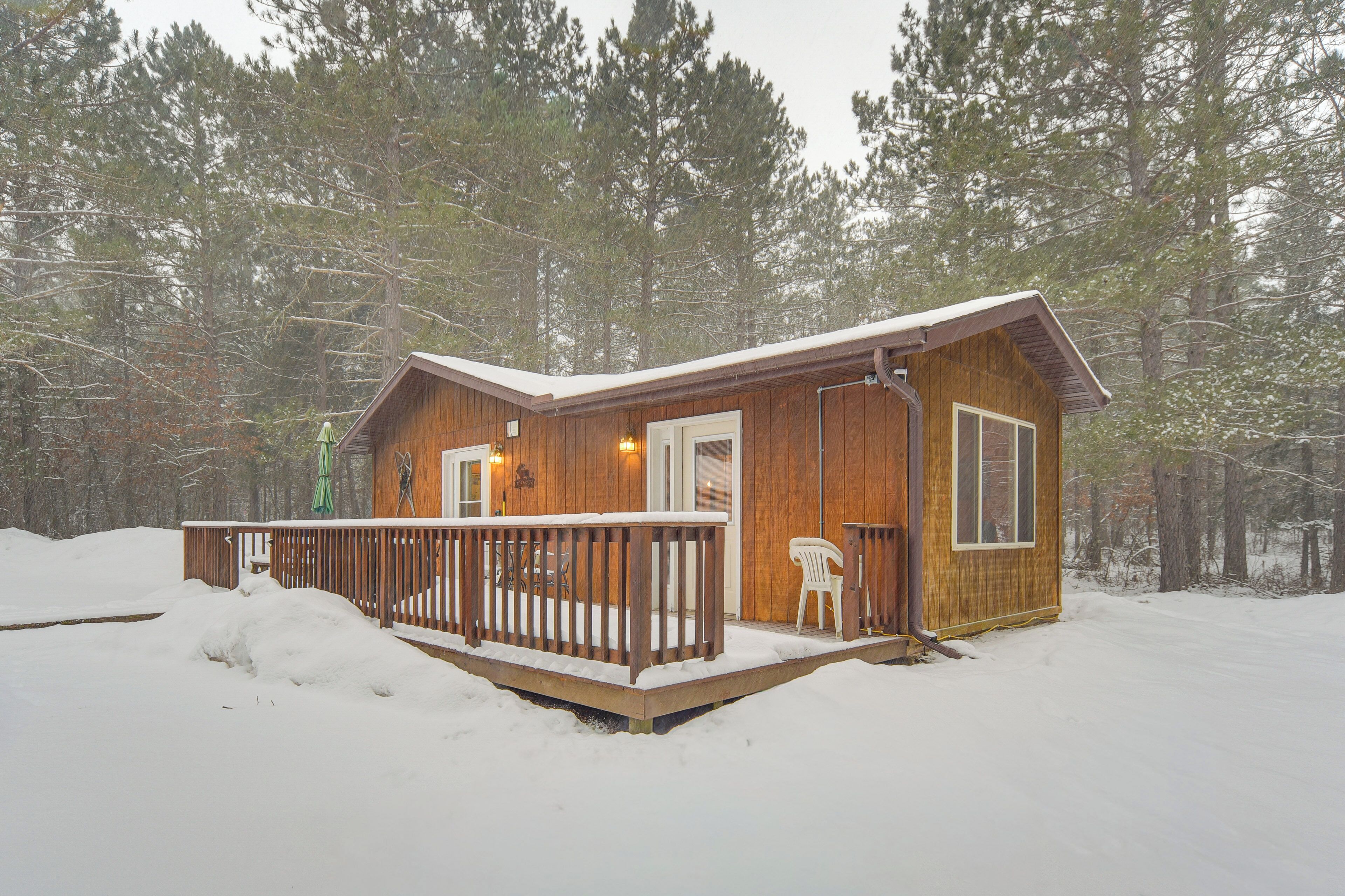 A wooden cabin with a deck, surrounded by snow and trees.