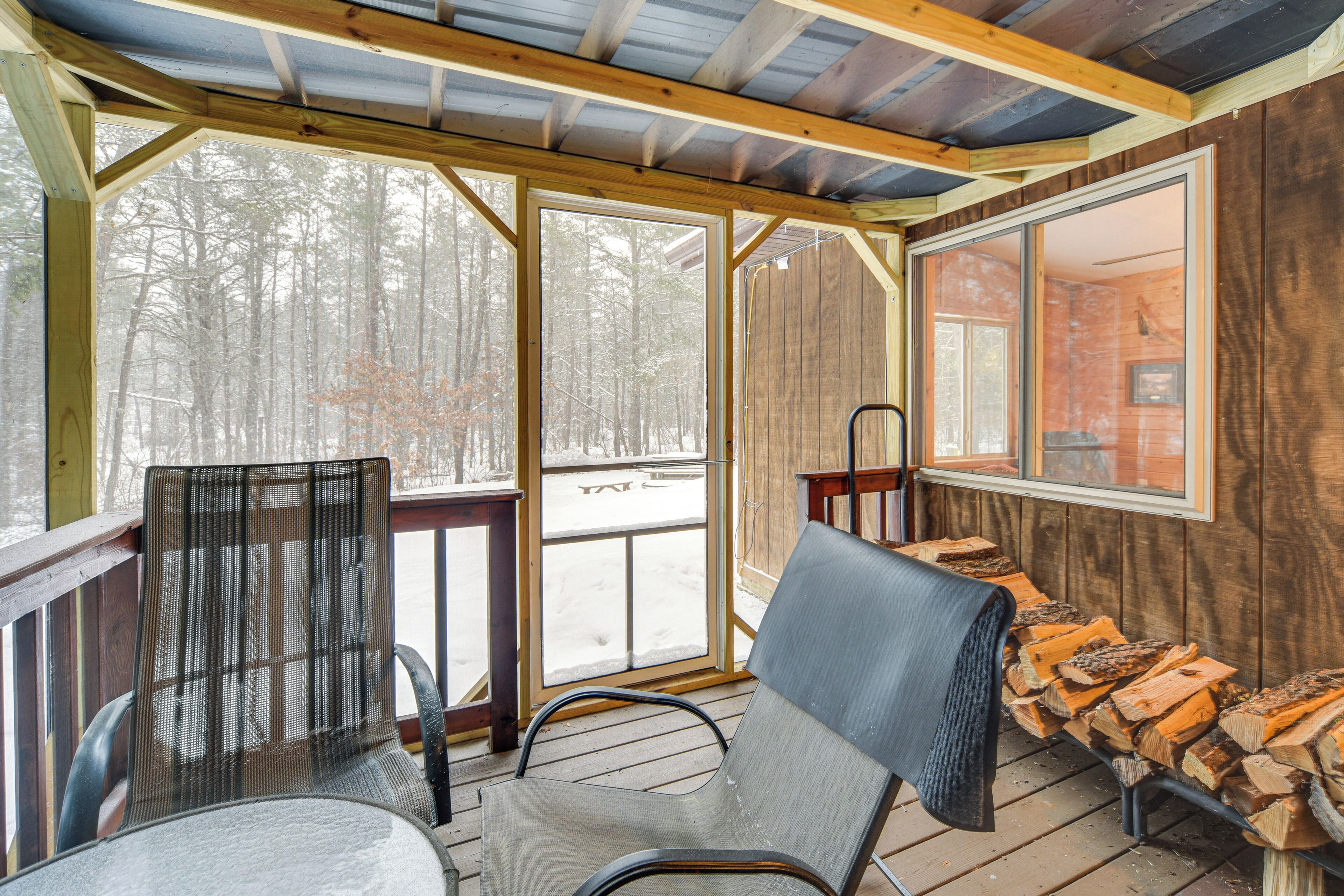Eine Holzterrasse mit Stühlen und einer Bank, große Fenster und Blick auf einen verschneiten Wald.