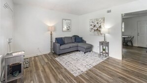 Un salon moderne avec un canapé d’angle gris, un tapis à motifs et une petite table d’appoint avec une lampe.