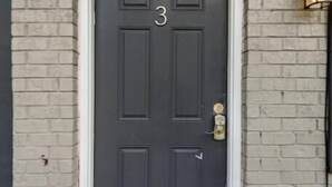 Une porte gris foncé portant le numéro 3, une sonnette en laiton et un luminaire fixé au mur.