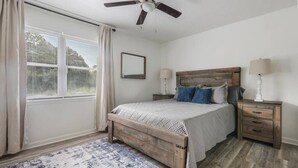 Une chambre à coucher avec un lit en bois, deux tables de chevet, un ventilateur de plafond et une fenêtre avec des rideaux.