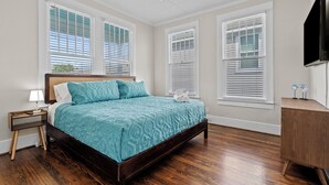 A bedroom with a wooden bed, white walls, and a ceiling fan. - Island Pride Coastal Cottage - 2 King Beds on the East End! (Galveston)