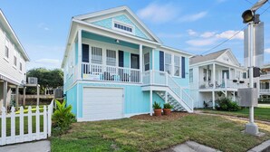 A two-story house with a front porch, a garage, and a small front yard. - Island Pride Coastal Cottage - 2 King Beds on the East End! (Galveston)