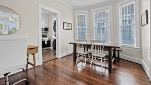 A dining area with a wooden table and chairs, a white ceiling fan, and a kitchen in the background. - Island Pride Coastal Cottage - 2 King Beds on the East End! (Galveston)