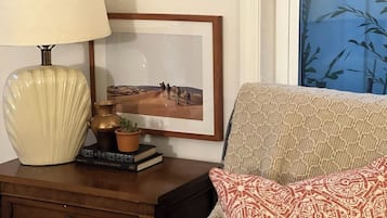 Une pièce comprenant une table de chevet en bois, une lampe, un tableau encadré, un canapé à motifs et une fenêtre donnant sur un paysage de bambous.