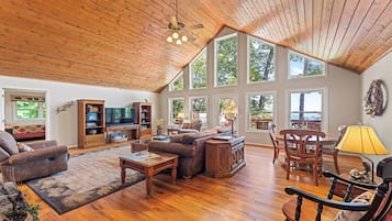 Un salon spacieux avec un plafond haut, un plancher en bois et de grandes fenêtres offrant une vue sur l’extérieur.