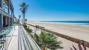 Un hôtel situé en bord de mer, doté d’un balcon offrant une vue sur l’océan, les palmiers et une plage de sable.